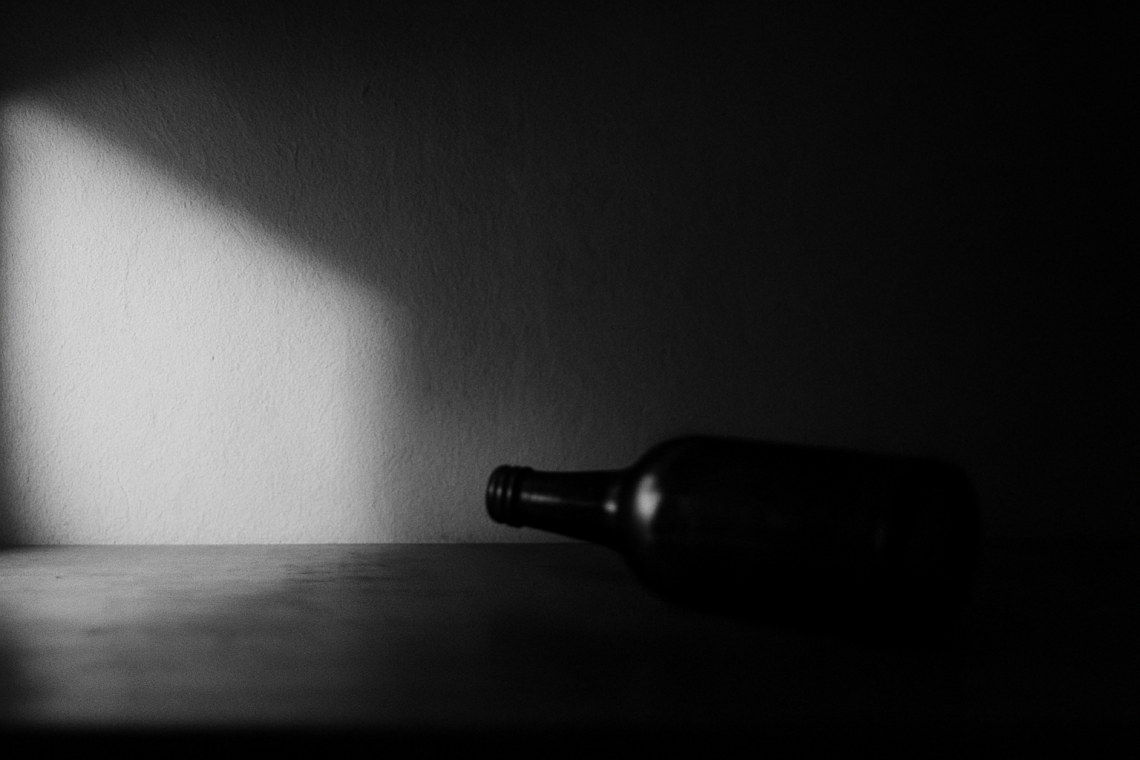 Schwarzweißfotografie einer unscharfen Flasche im harten Licht, als Symbol für den stillen Moment, in dem eine Alkoholabhängigkeit in der Beziehung erkennbar wird.