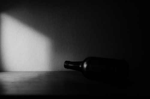 Schwarzweißfotografie einer unscharfen Flasche im harten Licht, als Symbol für den stillen Moment, in dem eine Alkoholabhängigkeit in der Beziehung erkennbar wird.